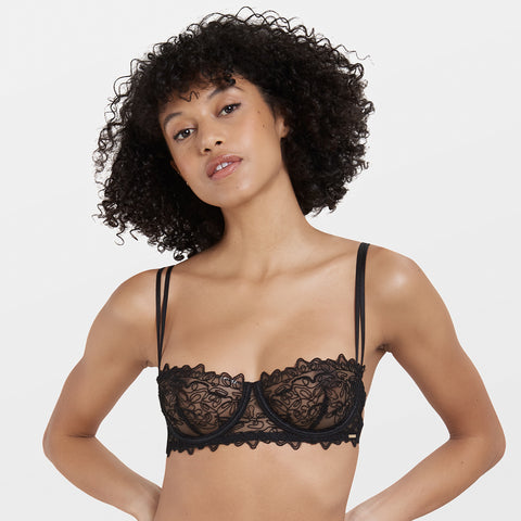 Model wearing Bluebella's Audrey balcony bra in black with embroidered sheer mesh and underwire support.